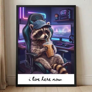 May include: A framed print featuring a raccoon wearing a hat and sunglasses, seated in a gaming chair, holding a drink with a straw. The background shows a gaming setup with monitors and neon lights. The text "i live here now" is at the bottom.