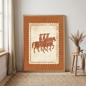 May include: A framed wall art print featuring a cream-colored postage stamp design on a solid terracotta background. The stamp illustration depicts three figures wearing wide-brimmed hats riding horses in profile, rendered in a dark brown line art.