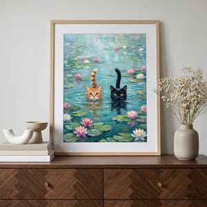 May include: A framed wall art print featuring an oil painting of an orange tabby cat and a black cat swimming in a pond filled with green lily pads and pink and white water lilies. The cats have their heads and tails visible above the water surface.