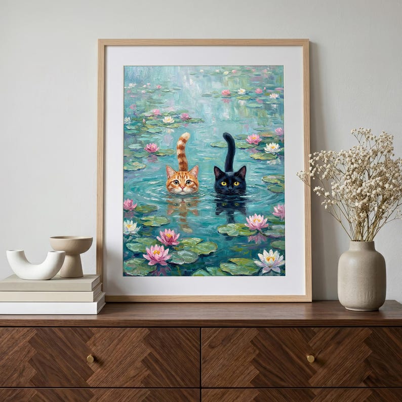 May include: A framed wall art print featuring an oil painting of an orange tabby cat and a black cat swimming in a pond filled with green lily pads and pink and white water lilies. The cats have their heads and tails visible above the water surface.