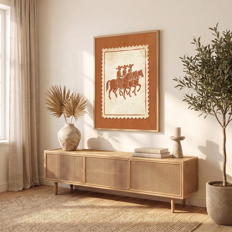 May include: A rectangular wall art print featuring a terracotta-colored background with a central cream-colored postage stamp design. The stamp depicts three figures in wide-brimmed hats riding horses in a line, rendered in a dark brown outline.