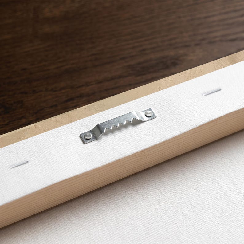 May include: A rectangular wooden frame with a white canvas backing. A silver-colored metal sawtooth hanger is securely attached to the center of the wooden frame with two small nails. The canvas is pulled taut and fastened with staples.