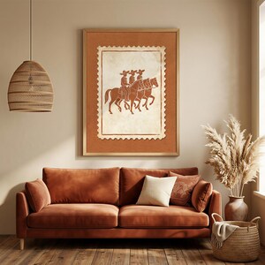 May include: A framed wall art print featuring a postage stamp design with a terracotta-colored illustration of three riders on horseback wearing sombreros. The artwork is displayed in a light wood frame against a solid, neutral-toned wall.