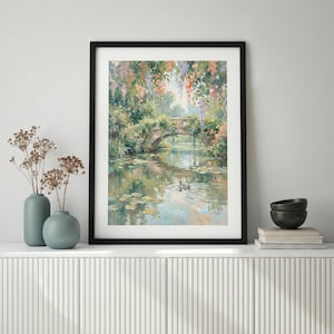 May include: A framed art print of a serene landscape featuring a stone bridge over a calm body of water. The painting showcases a bridge adorned with lush greenery and colorful flowers, with a duck swimming in the water. The artwork is framed in a black frame.