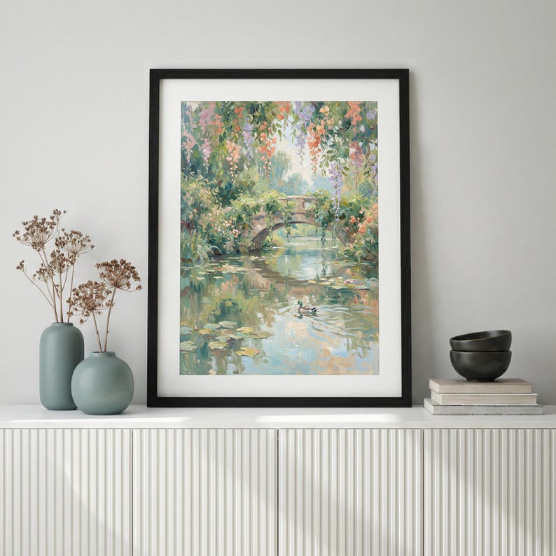 May include: A framed art print of a serene landscape featuring a stone bridge over a calm body of water. The painting showcases a bridge adorned with lush greenery and colorful flowers, with a duck swimming in the water. The artwork is framed in a black frame.