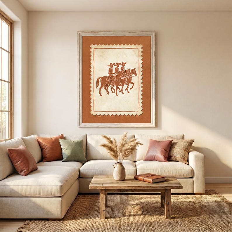 May include: A framed wall art print featuring a terracotta-colored postage stamp design with a white center. The illustration depicts three figures wearing wide-brimmed hats riding horses in profile, rendered in a simple, monochromatic line style.