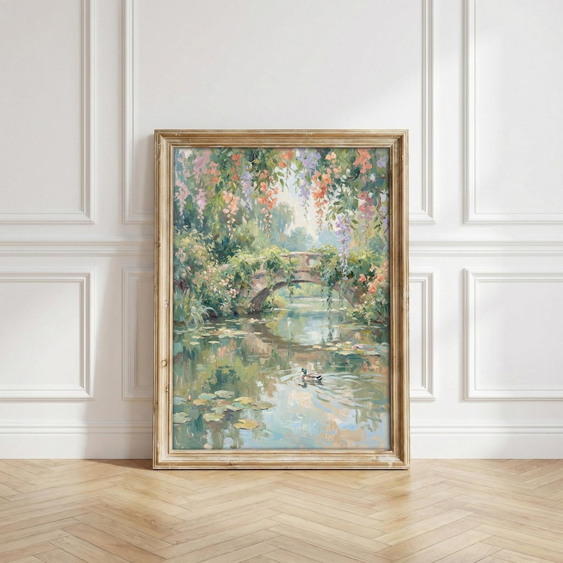 May include: A framed painting depicts a serene waterscape with a stone bridge. Lush greenery and colorful flowers cascade over the bridge and surrounding the water. The painting's soft colors and brushstrokes create a tranquil, impressionistic scene. A duck swims in the water.