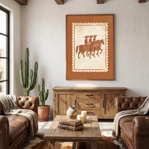 May include: A framed wall art print featuring a postage stamp design with a terracotta-colored illustration of three figures riding horses. The artwork is set against a solid terracotta background within a simple wooden frame.