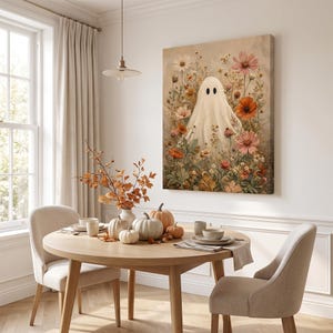 May include: A rectangular wall art print featuring a white ghost figure centered among a variety of colorful wildflowers in shades of orange, pink, and white. The artwork is displayed on a plain wall above a wooden dining table with pumpkins.