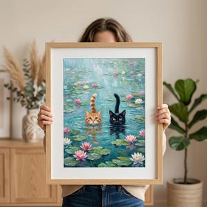 May include: A framed art print featuring an oil painting of an orange tabby cat and a black cat swimming in a pond filled with green lily pads and pink and white water lilies. The cats have their heads and tails visible above the water surface.