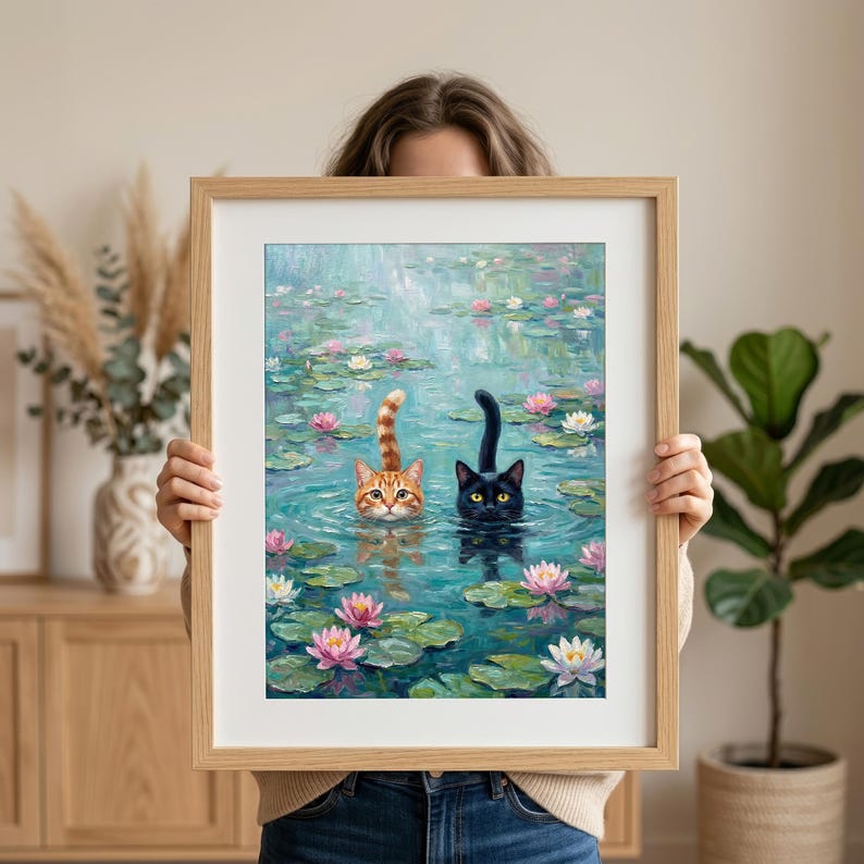 May include: A framed art print featuring an oil painting of an orange tabby cat and a black cat swimming in a pond filled with green lily pads and pink and white water lilies. The cats have their heads and tails visible above the water surface.