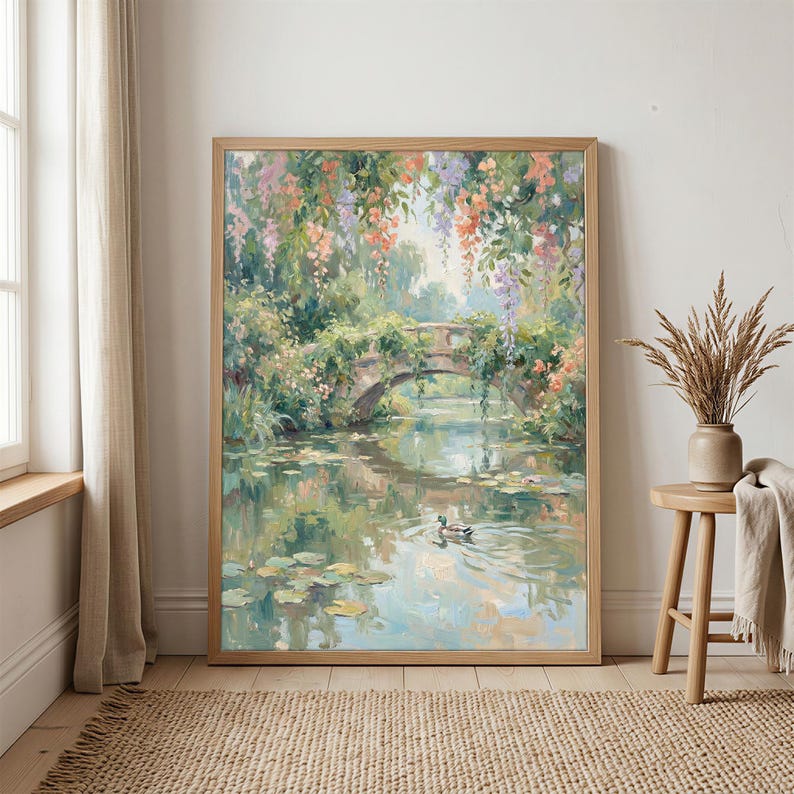 May include: A framed painting depicts a serene waterscape with a stone bridge, lush greenery, and colorful hanging flowers. A duck swims in the water, reflecting the sky and surrounding foliage. The artwork is in a wooden frame.