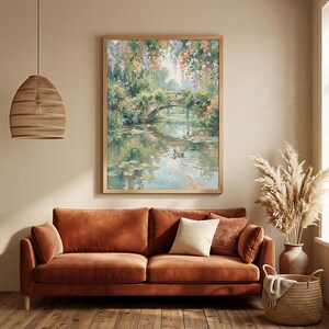 May include: A framed landscape painting depicts a stone bridge over a tranquil pond, surrounded by lush greenery and colorful flowers. The artwork is displayed above a rust-colored sofa with pillows, complemented by a woven pendant light and a decorative basket.