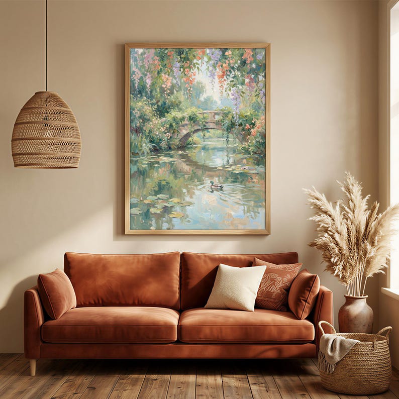 May include: A framed landscape painting depicts a stone bridge over a tranquil pond, surrounded by lush greenery and colorful flowers. The artwork is displayed above a rust-colored sofa with pillows, complemented by a woven pendant light and a decorative basket.