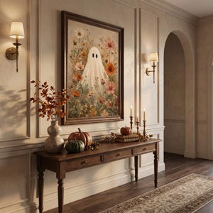 May include: A framed wall art print featuring a white ghost surrounded by a vibrant field of colorful wildflowers, including daisies and poppies, displayed above a wooden console table with pumpkins and a vase of autumn foliage.