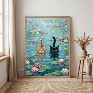 May include: A framed wall art print depicting an oil painting of an orange tabby cat and a black cat swimming in a pond filled with green lily pads and pink and white water lilies. The cats have their heads and tails visible above the water.