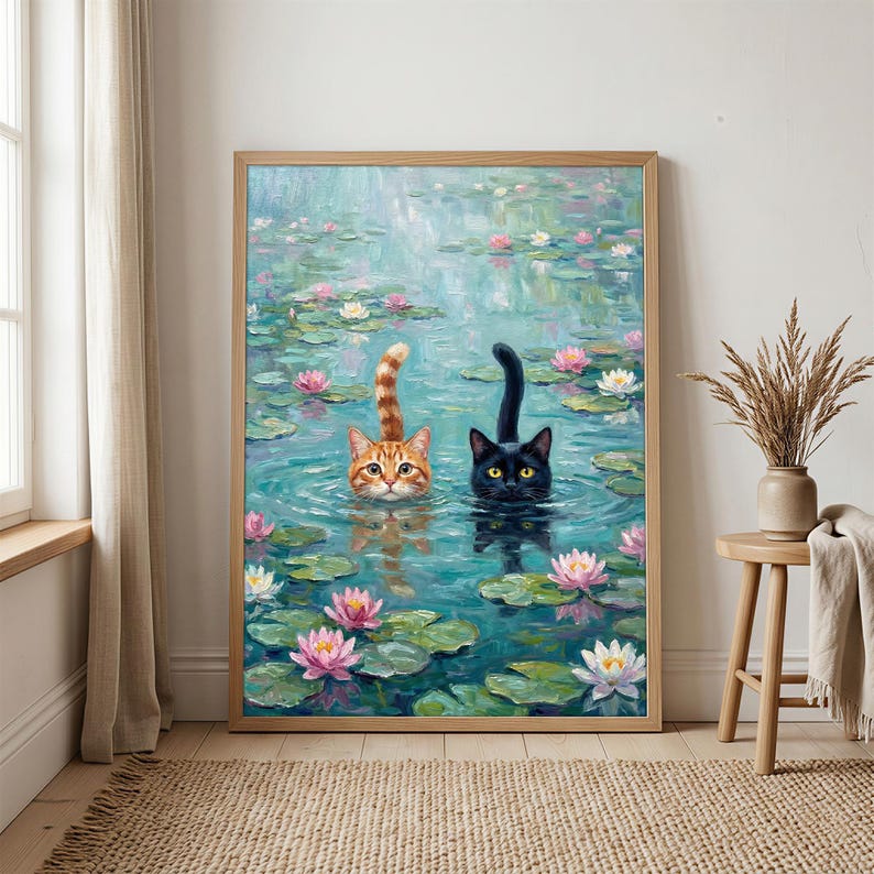 May include: A framed wall art print depicting an oil painting of an orange tabby cat and a black cat swimming in a pond filled with green lily pads and pink and white water lilies. The cats have their heads and tails visible above the water.