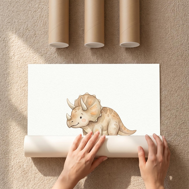 Puede incluir: Ilustraci&oacute;n en acuarela de un simp&aacute;tico dinosaurio Triceratops en tonos beige y marr&oacute;n. La obra de arte est&aacute; sobre papel blanco, parcialmente enrollado, con tres tubos de cart&oacute;n marr&oacute;n encima.
