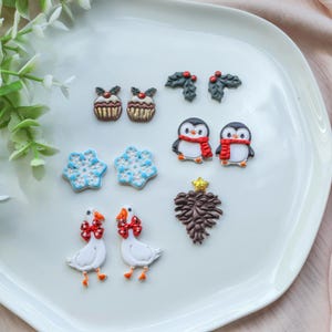 May include: A collection of Christmas-themed decorative items, including cupcakes, holly sprigs, penguins with red scarves, snowflakes, geese with red bows, and a brown pinecone with a gold star.