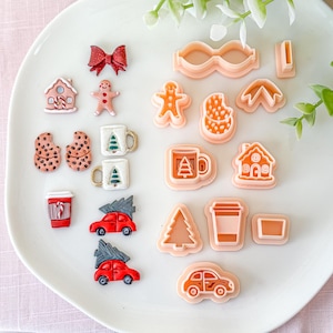 Può includere: Una collezione di formine per biscotti e elementi decorativi a tema natalizio. Include un fiocco rosso, omino di pan di zenzero, casa, tazze, biscotti, tazze da caffè e auto rosse con alberi di Natale. Le formine hanno varie forme.