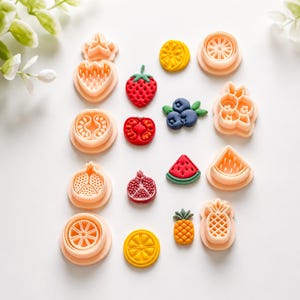 Può includere: Una collezione di tagliabiscotti in plastica color pesca a forma di frutta e le corrispondenti forme di frutta in argilla colorata, inclusi disegni di fragola, mirtillo, pomodoro, melograno, anguria, ananas e fette di agrumi.