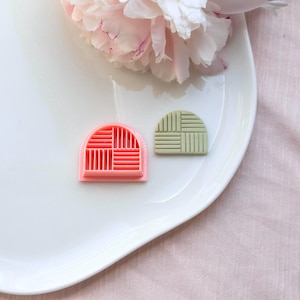 Könnte beinhalten: Zwei kleine, halbkreisförmige Ausstecher. Einer ist korallenfarben mit einem Gittermuster, der andere hellgrün mit einem ähnlichen Design. Die Ausstecher liegen auf einem weißen Teller, mit einer rosa Blume im Hintergrund.