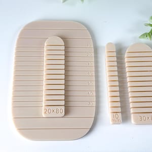 Può includere: Strumenti in argilla beige per ceramica o scultura. Il set include un grande strumento rettangolare con una guida di misurazione verticale e due strumenti più piccoli. Lo strumento grande ha le dimensioni 20x80, e lo strumento più piccolo ha le dimensioni 10 mm.