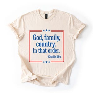 Puede incluir: Camiseta color crema con el texto "Dios, familia, país. En ese orden." en un diseño enmarcado en rojo y azul. El texto está atribuido a Charlie Kirk. La camiseta tiene cuello redondo y mangas cortas.