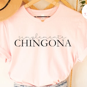 May include: Pink t-shirt with the text "simplemente CHINGONA" in black.