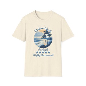 Puede incluir: Camiseta color crema con un gráfico circular de una escena de playa con palmeras, olas del océano y una puesta de sol. El texto "Madeira Islands Portugal" y "Highly Recommend" está impreso en azul.