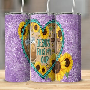 Puede incluir: Un vaso con purpurina morada con un diseño en forma de corazón con girasoles, una cruz y el texto "JESUS FILLS MY CUP". El vaso también tiene un dibujo de un café helado. El vaso tiene una pajita.