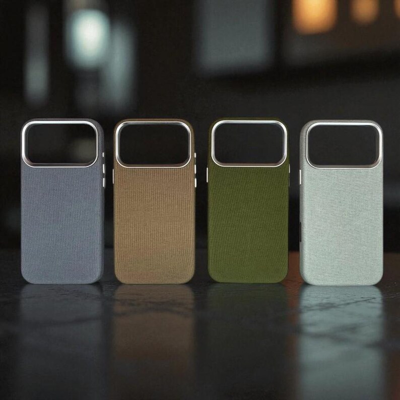 May include: Four mobile phone cases in a row, each with a different coloured fabric back. The colours are grey, tan, olive green, and light blue. Each case has a silver frame around the camera cutout.