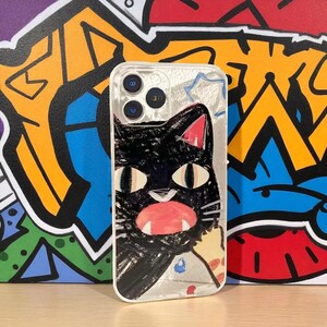 May include: Transparent phone case with a black cat design, pink ears, and a red mouth. The cat is depicted in a playful style, with big eyes and a fun expression. The case has a white edge and is set against a vibrant graffiti background.
