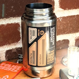 Könnte beinhalten: Eine Edelstahl-Wasserflasche mit den Aufschriften "HYDRATION SUPPORT" und "JOY CORP". Die Flasche hat Etiketten für "AERATION", "FILTRATION" und "HYDRATION". Ein QR-Code und der Code "BCP-0161-A" sind ebenfalls sichtbar.