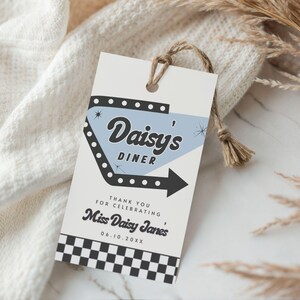 May include: A retro-style gift tag with the text "Daisy's Diner" in a stylized font, featuring a light blue arrow design. The tag includes the text "Thank you for celebrating Miss Daisy Janes" and a black and white checkered pattern.