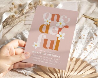 May include: A rectangular invitation card with a dusty pink background featuring the text "one der ful" in large, bold, white and orange letters, accented by white daisy illustrations. The card includes event details for Mila's 1st birthday.