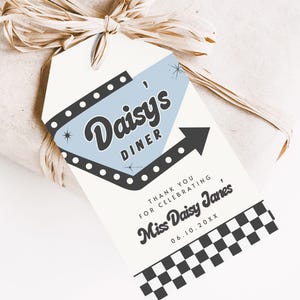 May include: A gift tag with a retro diner theme. The tag features the text "Daisy's Diner" in a stylized font, with a light blue background and a black arrow. The tag also includes the text "Thank you for celebrating, Miss Daisy Janes" and a checkered pattern.