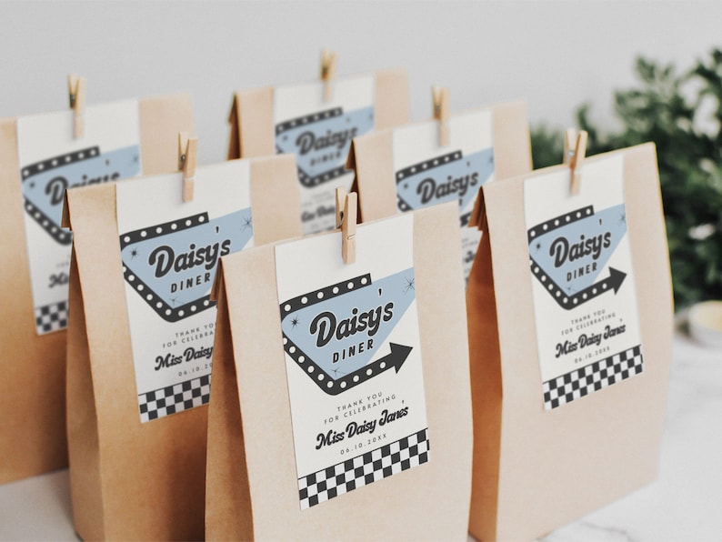 May include: Several kraft paper favor bags with tags that read "Daisy's Diner." The tags have a retro diner design in blue and black, with a black arrow. Each bag is clipped with a small wooden clothespin. The bags are for a celebration.