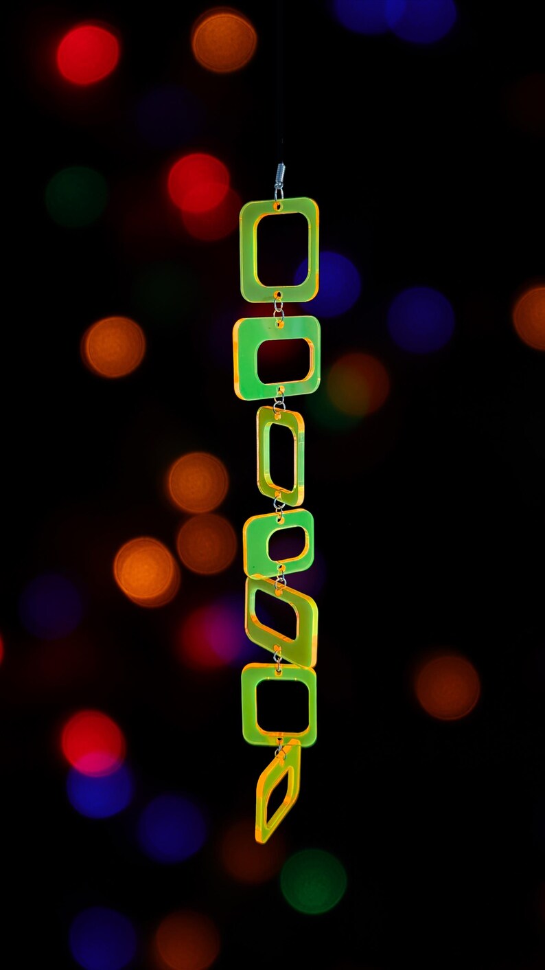 May include: A vertical chain of six translucent neon yellow-green square and rectangular acrylic links connected by small silver metal jump rings. The links are arranged in a descending line, creating a geometric pendant structure with a bright glow.