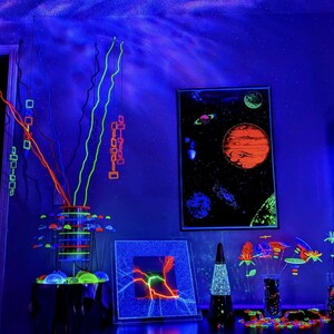 May include: A room interior illuminated by blue light featuring a space-themed poster, a lava lamp, a plasma disc, and several decorative arrangements of neon-coloured, glowing branches and floral shapes that emit a bright fluorescent light.