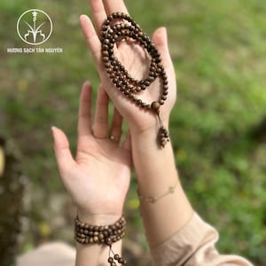 Könnte beinhalten: Ein Set aus Holzperlenketten und einem Armband. Die Perlen haben eine warme braune Farbe und scheinen auf einer Schnur aufgereiht zu sein. Die Halsketten werden in der Hand gehalten, und das Armband wird am Handgelenk getragen.