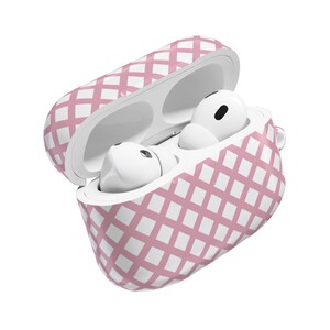 May include: An open, pink and white patterned case containing white wireless earbuds. The case has a grid-like design and a small loop for attaching to a keychain or bag. The earbuds are visible inside the case.