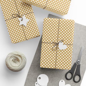 May include: Overhead view of wrapped presents with a gold and white grid design. Each gift is tied with string and has a white tag. A ball of string, scissors, and extra tags are also visible.