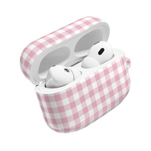 May include: A pink and white gingham-patterned case for wireless earbuds. The case is open, showing two white earbuds. The case has a smooth, glossy finish and a small loop on the side.