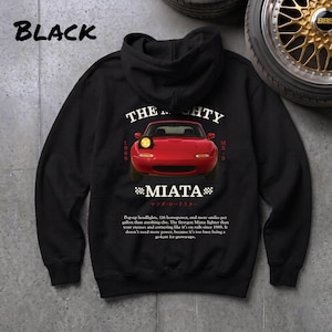 May include: Black hoodie with a red Miata car graphic, text reading "THE MIGHTY MIATA" and "1989 MX-5". The hoodie also has text about the car's features. The word "BLACK" is printed at the top.