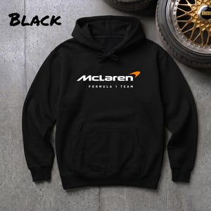 Può includere: Felpa con cappuccio nera con il logo McLaren Formula 1 Team in bianco e arancione. La parola "BLACK" è stampata in bianco in alto a sinistra. La felpa ha una tasca frontale e un cappuccio con coulisse.