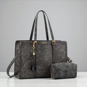 Puede incluir: Un conjunto de bolso tote y neceser a juego de color gris oscuro. El tote presenta un diseño floral en relieve, asas superiores, una correa para el hombro y herrajes dorados. El neceser tiene cierre de cremallera. La marca "Lavoach" es visible.