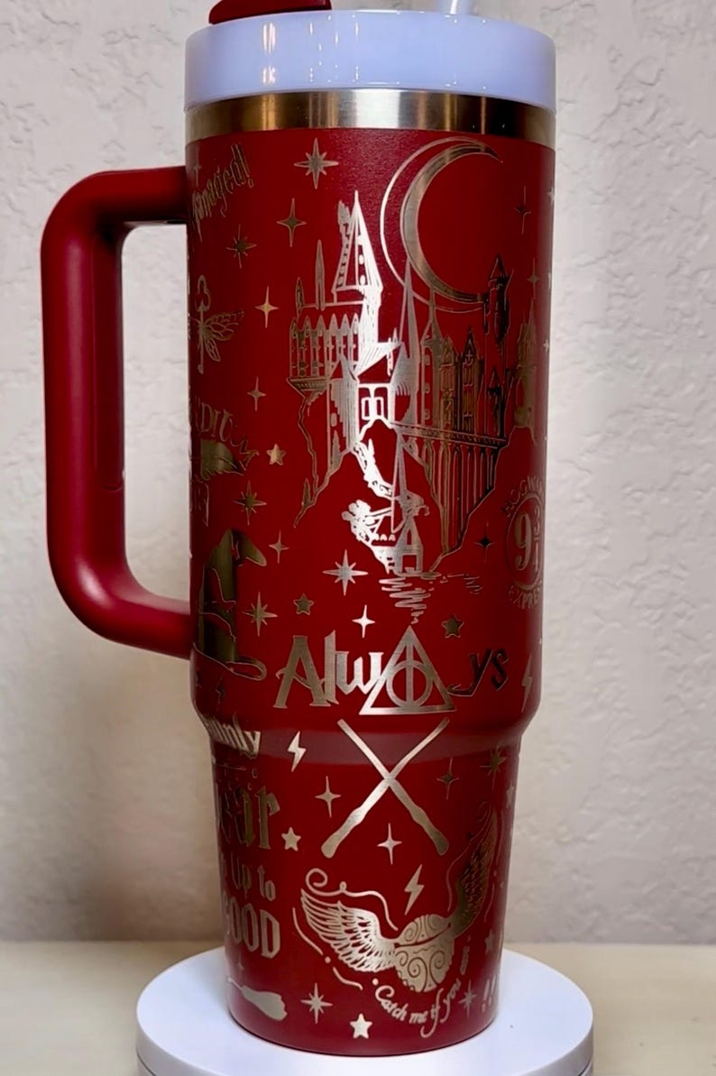 Puede incluir: Un vaso t&eacute;rmico rojo con asa, con un dise&ntilde;o plateado de un castillo, estrellas y texto. El vaso incluye las palabras "Always" y "Catch me if you can". La tapa es blanca y el asa es roja.