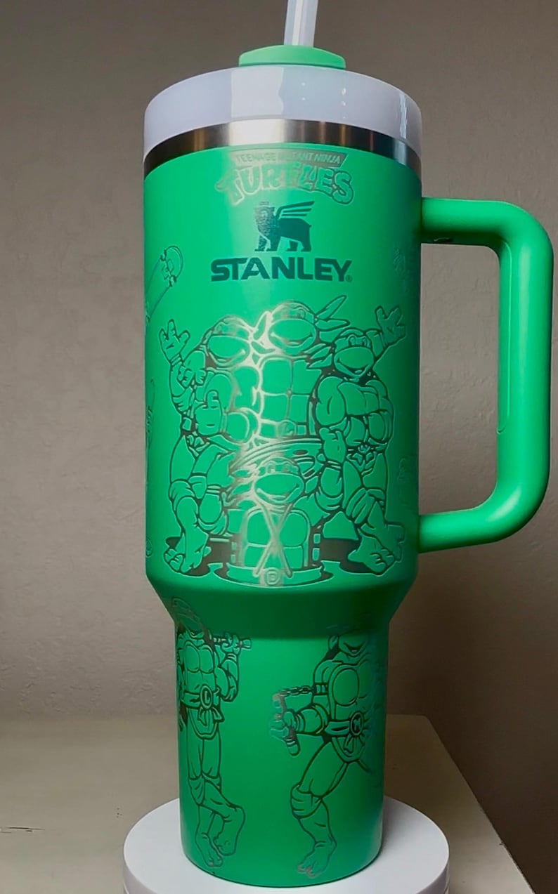Pu&ograve; includere: Bicchiere Stanley verde con grafica dei Tartarughe Ninja. Il bicchiere ha un coperchio bianco e argento, un manico verde e una cannuccia. Il design include le Tartarughe e il logo Stanley. Questo bicchiere isolato &egrave; ideale per bevande fredde.