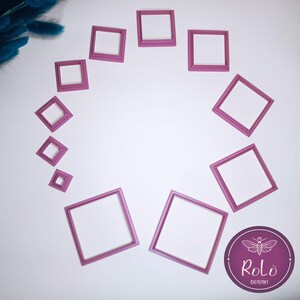 Può includere: Una collezione di cornici quadrate rosa di varie dimensioni disposte a cerchio. Le cornici sono vuote, con uno sfondo bianco visibile attraverso le aperture. Un cerchio viola con il testo "Rolo Design" è in basso a destra.